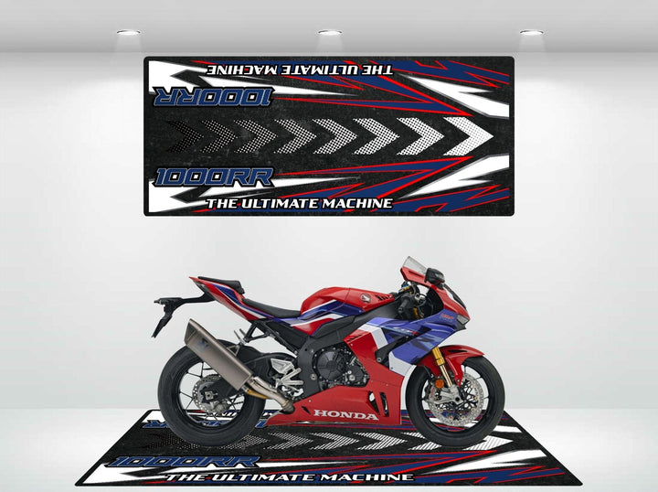 A red and blue Honda motorcycle is showcased in a showroom atop a sleek Motorcycle Pit Mat designed for the CBR1000RR, with The Ultimate Machine and 1000RR graphics adorning the walls and floor.